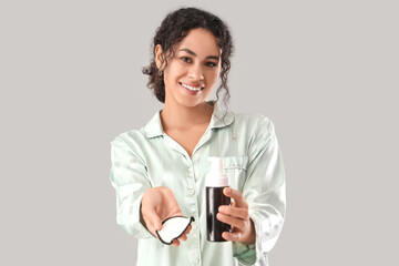 Beautiful young African-American woman with bottle of micellar water and pad on grey background