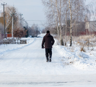 A man is walking on a snowy road in a rural area - Powered by Adobe
