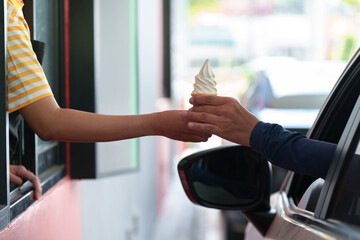 A man receives an ice cream burger and snacks in his car during rush hour from a female valet at the drive-thru lane..