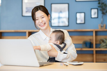 赤ちゃんを抱えてノートパソコンを操作する女性 © TAGSTOCK2