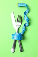 Blue tape measure with cutlery on color background, top view.