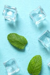 Top view photo of mint leaves, ice cubes and water drops on pastel blue background