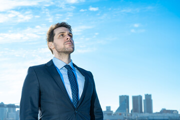 青空とビル群を背景にしたビジネスマンのポートレート