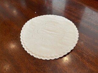 A Closeup View of an Off-White Scalloped Edge Coaster on a Dark Brown Wooden Surface