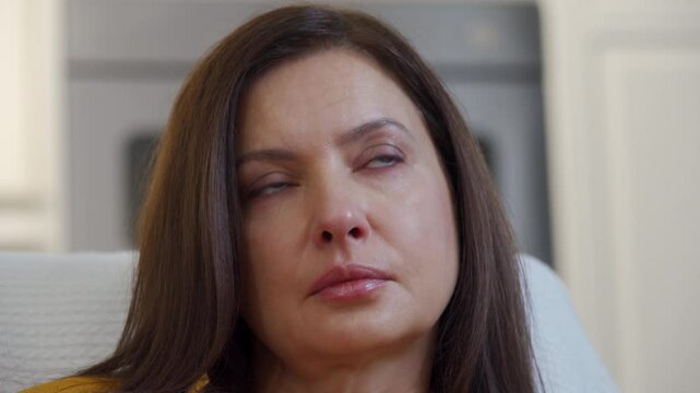Adult 44 year old woman sitting on sofa in living room in front of TV watching melodrama. Impressionable woman cries wiping tears worried while watching movie.
