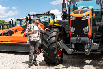 Caucasian man with digital tablet standing outdoors next to construction and agricultural machinery...