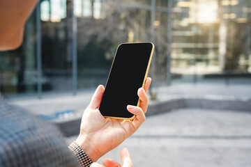 Smartphone with blank black screen in hand of businesswoman on city street.