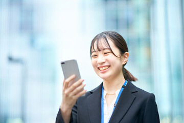Obraz premium スマートフォンの画面を見るスーツ姿の若い女性