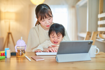 自宅でタブレットPCを操作する女性と泣く幼児