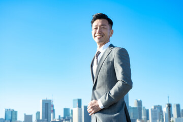 青空とビル群を背景にしたビジネスマンのポートレート