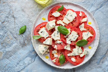 Plate with tomato and blue cheese salad, horizontal shot on a blue and beige stone background, high angle view