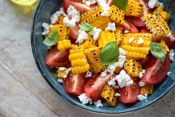 Close-up of salad with red tomatoes, grilled corn and cheese served in a blue bowl, horizontal shot