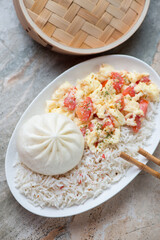 Plate with steamed rice, baozi and tomato egg-stir fry, vertical shot on a grey and roseate granite surface, middle close-up