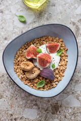 Granola bowl with yogurt, fresh and dried figs, vertical shot on a light-brown granite background, selective focus