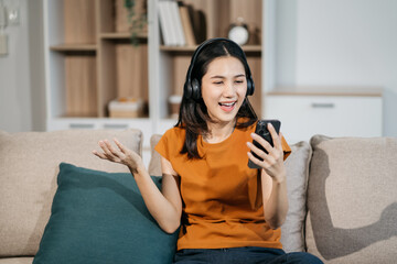 Happy woman having fun doing video call using mobile phone and Laptop sitting on sofa, home office workplace lifestyle people.