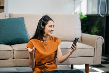 Happy woman having fun doing video call using mobile phone and Laptop sitting on sofa, home office workplace lifestyle people.