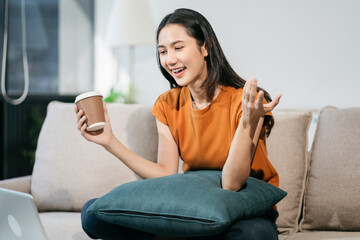 Obraz premium Happy woman having fun doing video call using mobile phone and Laptop sitting on sofa, home office workplace lifestyle people.