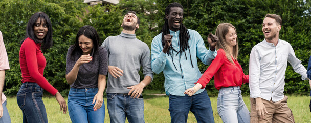 Diverse group of young friends dancing and laughing together in summer park