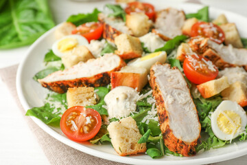 Tasty Caesar salad with chicken and tomatoes on white wooden table, closeup