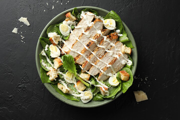 Delicious Caesar salad with chicken on black textured table, top view