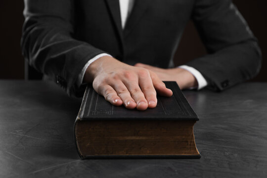 Man taking oath with his hand on Bible at black table, closeup - Powered by Adobe
