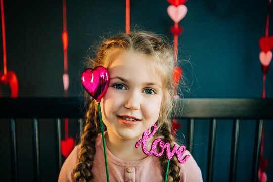 Smiling girl with braided hair holding "love" and heart props