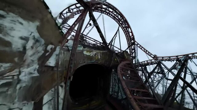 Rusty rollercoaster tracks wind through an abandoned amusement park, leading into a shadowy tunnel decorated with peeling graffiti