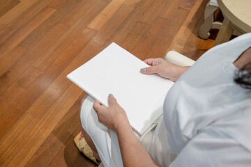 unrecognizable woman holding blank magazine for mockup design, sitting in chair