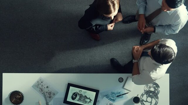 Top down view of smart engineer talking about turbine engine design while standing at meeting table with gear. Aerial view of technician discussing and shaking hand or making a contract. Alimentation.