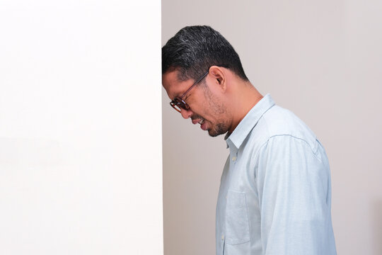 A man put his head on the wall showing stress expression