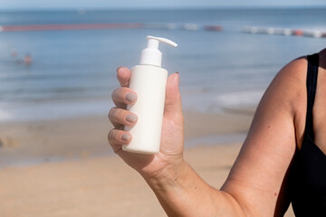 Woman putting sunblock lotion on shoulder before tanning during summer holiday on beach.