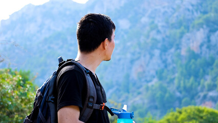 Young explorer man with backpack looking at mountains in the background on a sunny day