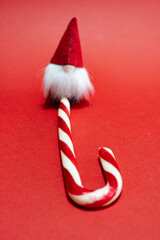 Small Christmas gnome with candy cane isolated on a red background. Christmas and Christmas concept.