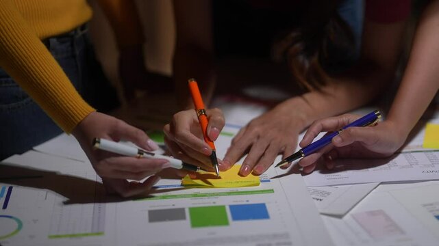A group of people are writing on a table with pens and markers. Scene is collaborative and focused, as the people are working together to create something