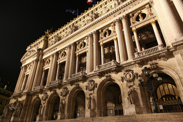 The iconic facade of the Palais Garnier Opera House in Paris, illuminated at night, showcasing its...