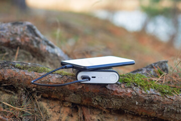 A portable charger charges the smartphone. Power Bank with cable in the forest.