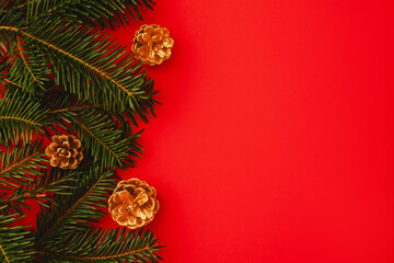 red christmas background. Minimalist Christmas arrangement with fresh evergreen branches and golden pinecones on a vibrant red background, perfect for holiday designs.