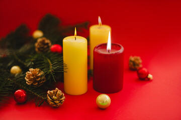 Festive holiday scene featuring glowing candles, evergreen branches, golden pinecones, and red ornaments on a bold red backdrop