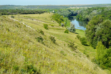 Expansive grassy hills and a winding river with surrounding trees, showcasing a peaceful natural...
