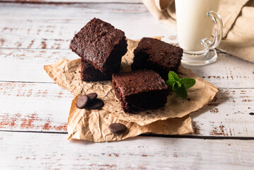Many pieces of fresh chocolate brownie sprinkled with cocoa on a  bakery paper with glass of milk...