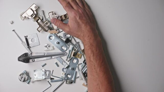 Close-up of screws, dowels, and hinges on a white table, hands organizing pieces for assembly, captured with a macro lens during the sorting process.