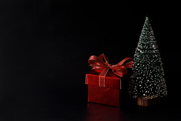 Miniature Christmas tree with red present box on black background.