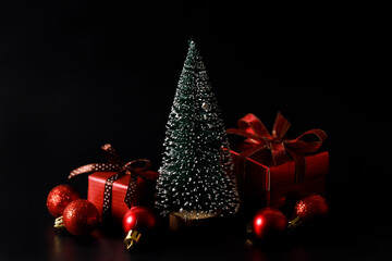 Miniature Christmas tree with red present boxes on black background.