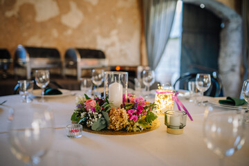 A beautifully set table with a floral centerpiece, a candle in a glass holder, and elegant tableware in a cozy rustic venue..