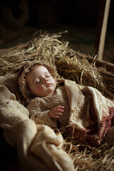 Baby Jesus Christ sleeping in a manger on straw. Newborn beautiful baby boy sleeping in straw and wrapped in old sackcloth swaddling clothes