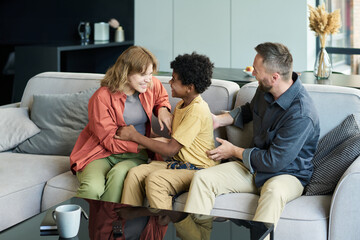 Obraz premium Multiracial family sitting on a comfortable couch in a modern living room, sharing smiles and engaging in conversation, demonstrating warmth and connection