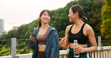 Fitness, happy friends and girls walking at park, talking or communication on phone. Japanese women, sports and outdoor together for body health conversation, exercise or gossip on break with bottle