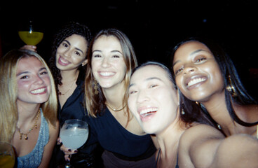 A group of happy friends posing together in a lively atmosphere, captured with a vintage film look,...