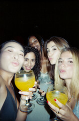 A joyful group of friends posing with drinks, captured with a film camera for a vintage and...