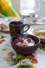 Sweet dumplings (vareniki) garnished with frozen raspberries, served in a rustic wooden bowl. The cozy setting highlights the dish's warmth, ideal for food photography or traditional dessert concepts